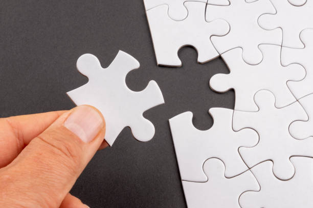 istock Fingers holding last missing jigsaw puzzle piece over black background. 1386951004