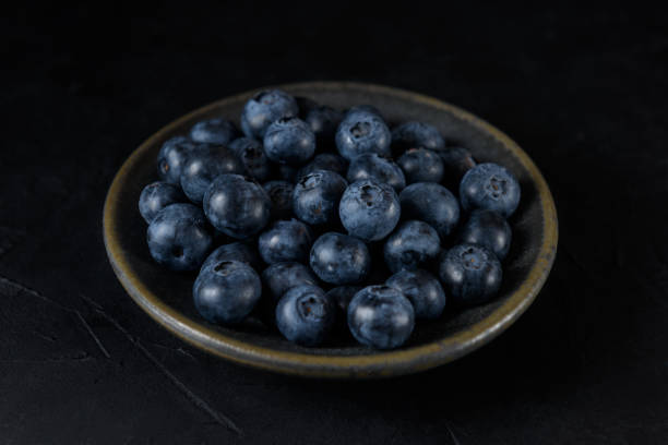 istock Fresh organic blueberries in a ceramic saucer on a black background 1386953286