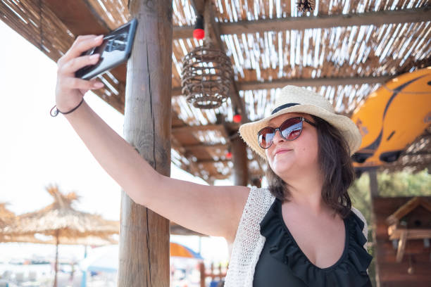 молодая жизнерадостная женщина делает селфи в баре на пляже - vacations photographing brown hair 30s стоковые фото и изображ�ения