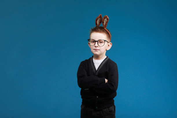 felizes crianças da páscoa. menino criança em orelhas coelho coelho na cabeça com óculos no fundo do estúdio azul. olhando e sorrindo para a câmera - face paint child paint rabbit - fotografias e filmes do acervo