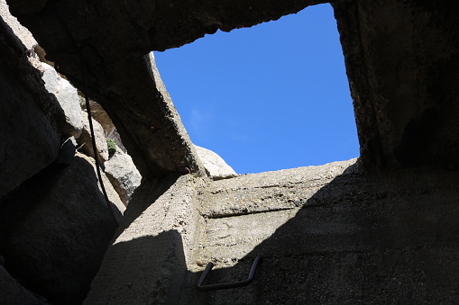 view of cloudless blue sky across a square hole from inside a broken concrete underground bunker