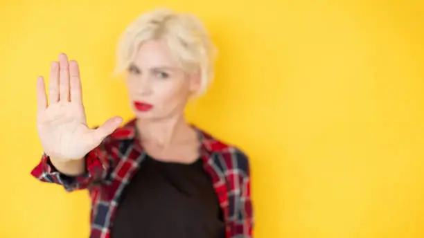 Stay out. Refusal woman. Keep distance. Defocused strict confident blonde lady showing forbidden gesture in protest isolated yellow copy space.