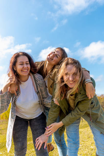 three diverse girlfriends are having fun and hugging. blue sky background. - group of objects travel friendship women imagens e fotografias de stock