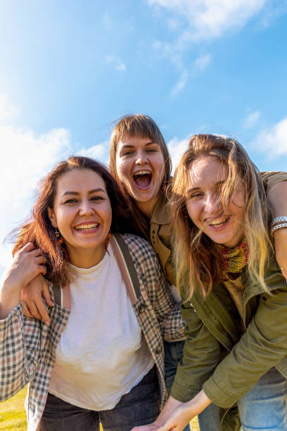 istock Three diverse girlfriends are having fun and hugging. Blue sky background. 1386976286
