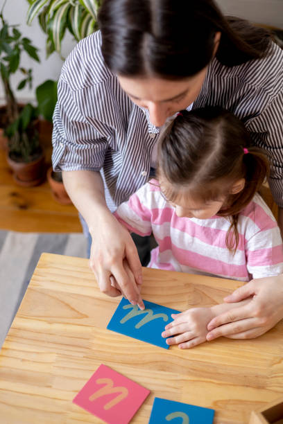 istock Montessori material. Mom helps her daughter learn letters using the rough alphabet. 1386977920