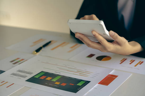 Asian businessman's hand is pressing calculator and preparing data while holding pen in finger to calculate, analyze investment advisor chart. and auditors to calculate the cost with a laptop la mano del empresario asiático está presionando la calculadora y preparando los datos mientras sostiene el bolígrafo en el dedo para calcular, analizar el gráfico del asesor de inversiones. y auditores para calcular el costo con una computadora portá