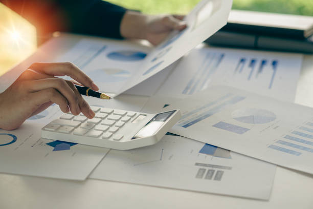 istock Asian businessman's hand is pressing calculator and preparing data while holding pen in finger to calculate, analyze investment advisor chart. and auditors to calculate the cost with a laptop 1386978326