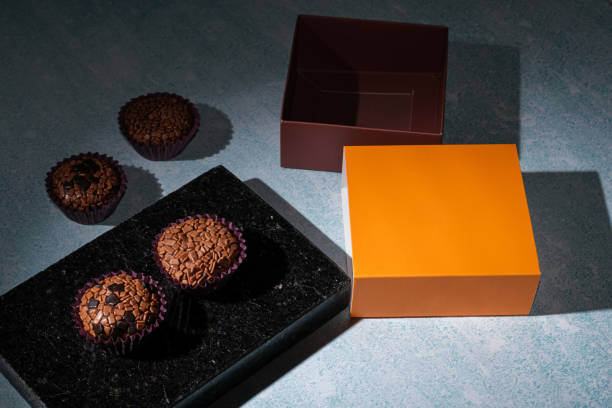 low key photo. brigadiers on a shiny black marble stone, next to an orange box lid. - craft chocolate candy black box imagens e fotografias de stock