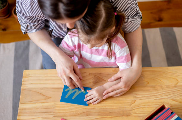 Montessori material. Mom helps her daughter learn letters using the rough alphabet.