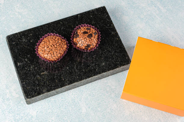 traditional and bitter brigadeiros on a black marble stone, next to an orange box. - craft chocolate candy black box imagens e fotografias de stock