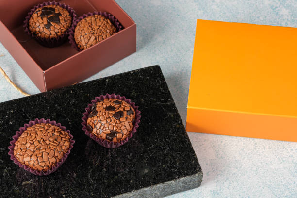 traditional and bitter brigadeiros on a black marble stone, next to an orange box. - craft chocolate candy black box imagens e fotografias de stock