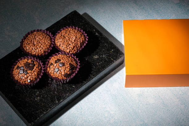 low key photo. brigadeiros arranged on a shiny black marble stone, next to an orange box. - craft chocolate candy black box imagens e fotografias de stock