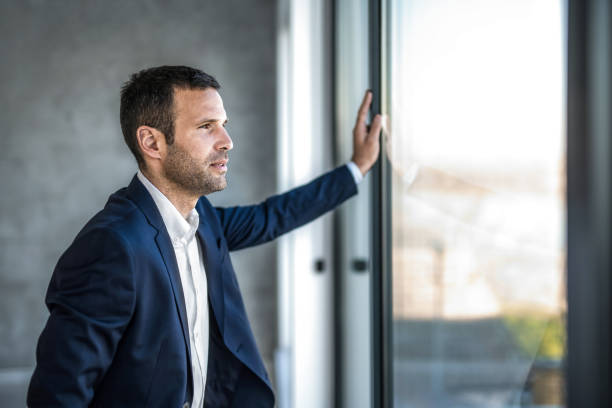 istock Handsome businessman looking through window and contemplating in the office. 1386984377