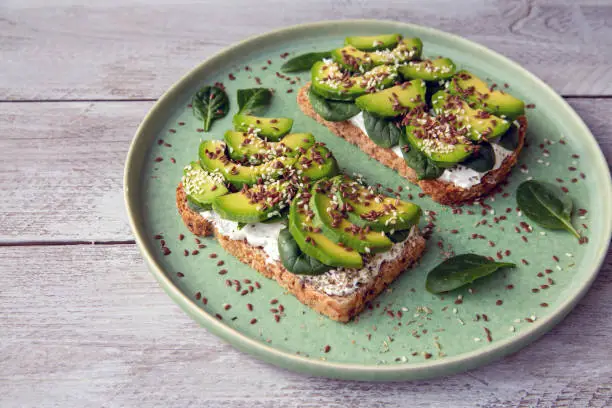 Toast with avocado, cottage cheese, spinach, sesame seeds, flax seeds. Healthy food rich in fiber, trace elements, omega acids, unsaturated lipids.