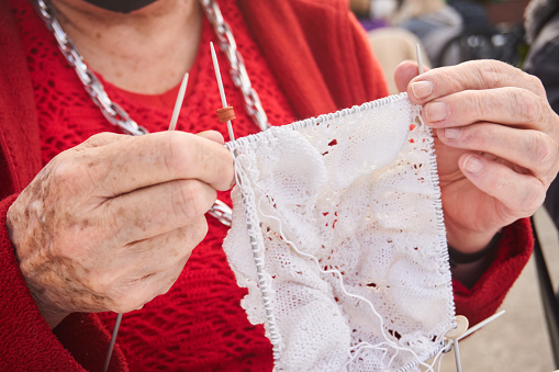 close-up of elderly woman embroidering a white artistic fabric with five needles and thread