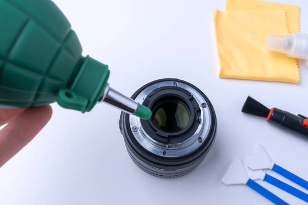 istock Photographer blows bullets from the camera lens. Camera cleaning accessories on white background 1387000052