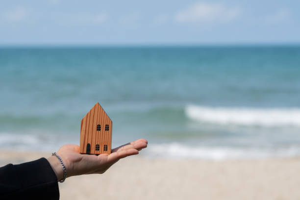 istock small home model on hand with sea background, miniature house 1387000072