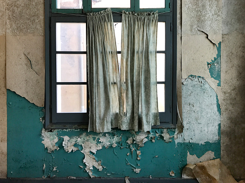 Detail of aged tattered old curtains across the window of a room in an abandoned former industrial warehouse in Spain