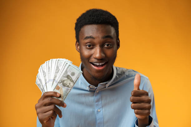 istock Excited black guy holding stack of Dollars in yellow studio 1387010851