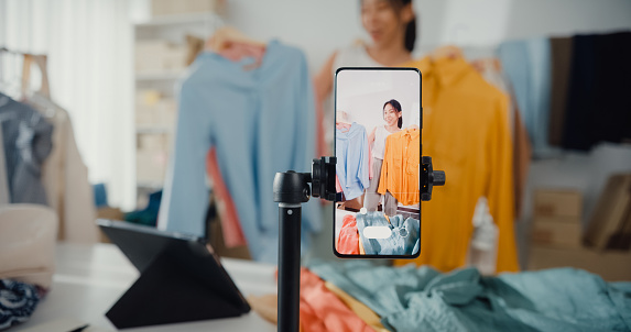 La empresaria asiática transmite en vivo el comercio electrónico vende ropa en casa, una chica hermosa que usa el teléfono inteligente y la tableta para grabar videos. photo