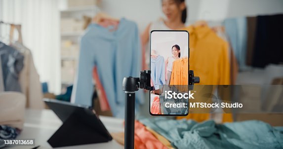 istock Asian businesswoman live-streamed ecommerce sell clothes at home, beautiful girl using the smartphone and tablet for recording video. 1387013658
