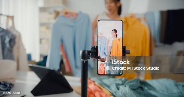 Asian Businesswoman Livestreamed Ecommerce Sell Clothes At Home Beautiful Girl Using The Smartphone And Tablet For Recording Video Stock Photo - Download Image Now