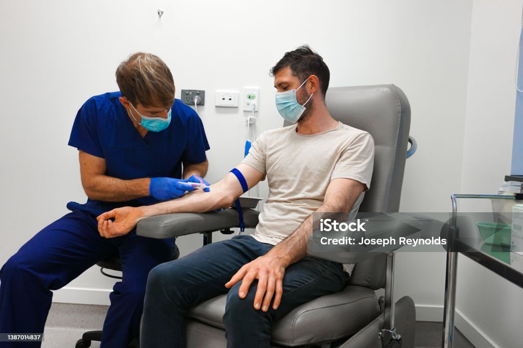 A patient having blood taken by a healthcare professional A patient sitting in a chair in a clinic room having blood taken from their right arm by a healthcare professional in blue gloves and medical scrubs Blood Donation Stock Photo