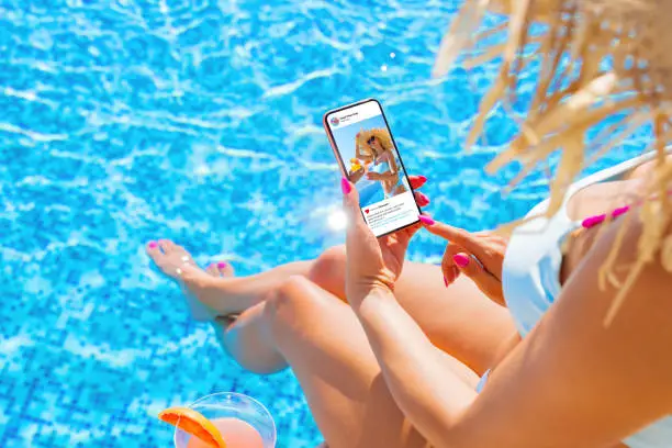 Photo of Woman using video sharing social media app on mobile phone while sitting by the pool