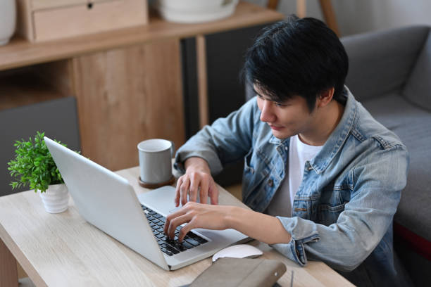 istock Young man sitting in living room and searching information, checking email on laptop computer. 1387023252