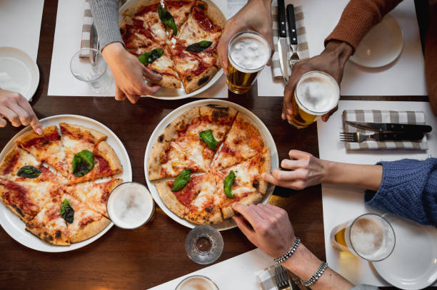 stół z widokiem na górę z nierozpoznawalną wielorasową grupą ludzi chwytających kawałek pysznej włoskiej pizzy i szklanki piwa. - pizza pizzeria friendship people zdjęcia i obrazy z banku zdjęć