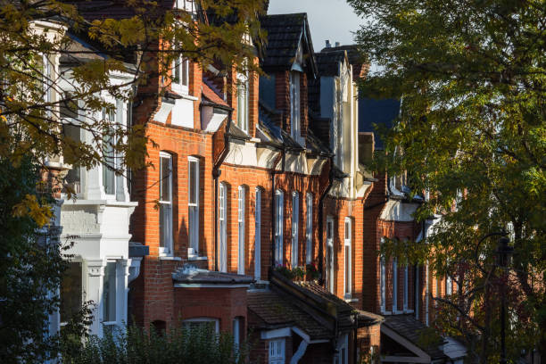 Facade of traditional English terraced houses partially in the shade of trees in London stock photo