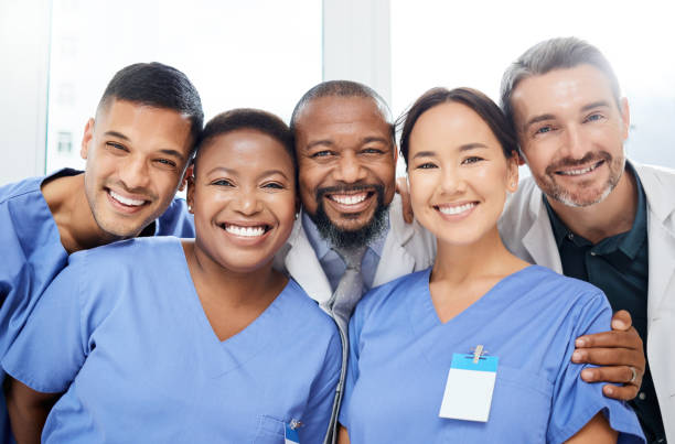 日中、病院内で腕を組んで立っている陽気な医師グループのショット - 医療従事者 ストックフォトと画像