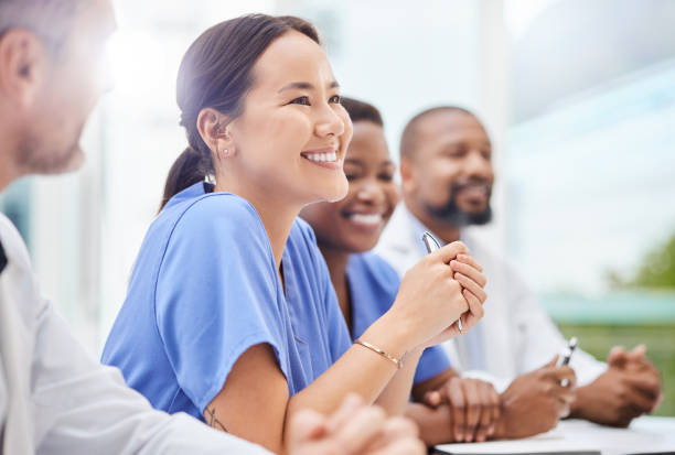 foto de un médico sentado junto a sus colegas durante una reunión en la sala de juntas de un hospital - women mature adult working doctor fotografías e imágenes de stock