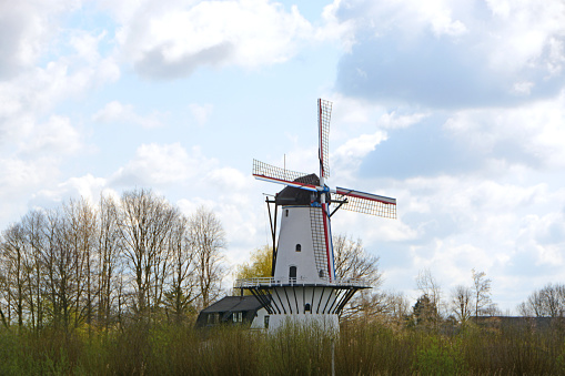 Single white windmill standing in a landscape, white treelinend bare trees.