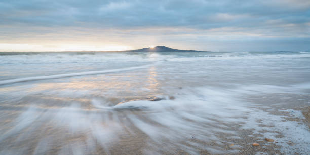 Sunrise at Rangitoto Island, slow movement of sea waves at foreground, Milford beach, Auckland. Sunrise at Rangitoto Island, slow movement of sea waves at foreground, Milford beach, Auckland. rangitoto island stock pictures, royalty-free photos & images