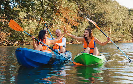 Kayaking at th river. A group of happy friends are high five sitting in kayaks. World Tourism Day concept.