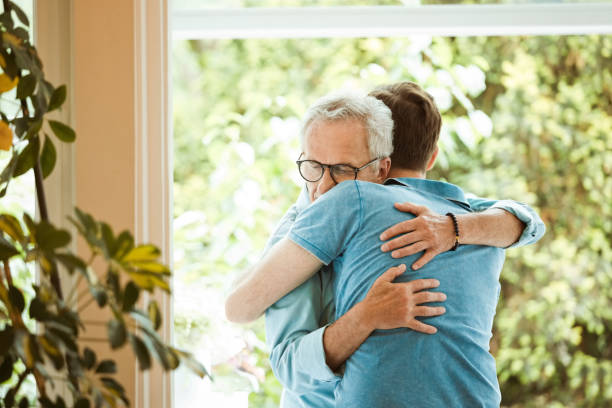 istock Senior man hugging son against window at home 1387039356