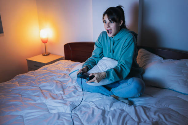 istock Woman having fun playing video games in bed at night 1387040964