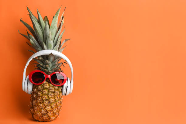 istock Pineapple with sunglasses and headphones on orange background, space for text. Creative concept 1387046961