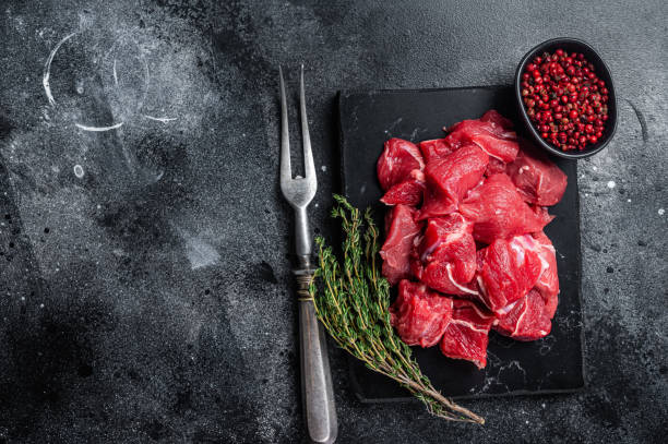 istock Raw diced red beef meat for Goulash on marble board. Black background. Top view. Copy space 1387048339