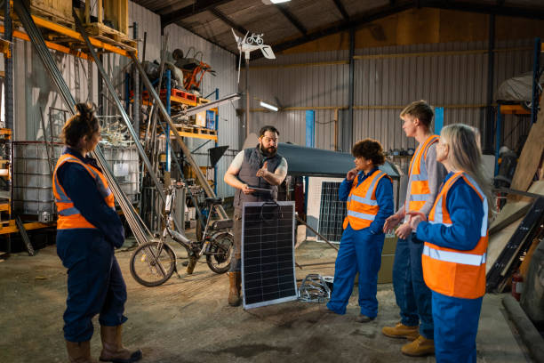 Breaking New Ground Team standing talking and learning together. The company uses renewable/sustainable energy and resources in the North East of England. They are working on an electric bicycle, holding a solar panel. resourceful stock pictures, royalty-free photos & images