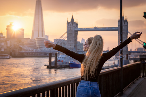 A happy tourist woman stands in front of the Tower Bridge in London during sunset time and enjoys the view