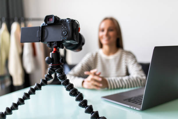 istock Confident young female vlogger sit at desk shooting live broadcast on professional camera. successful girl speaker or coach talk speak record video tutorial or blog at home 1387048773
