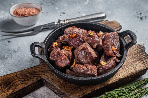 carne de res salteada a la parrilla en cubitos en una sartén con ajo. fondo gris. vista superior - sirloin steak fotografías e imágenes de stock