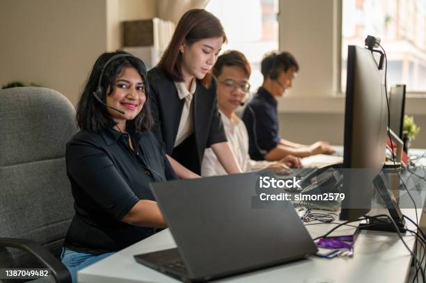 Young Asian Call Center Operator Woman In Headset Working On Computer And Looking At Camera Stock Photo - Download Image Now