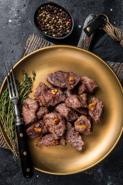 istock Chopped Grilled Diced Beef garlic steak on a plate with thyme. Black background. Top view 1387049524