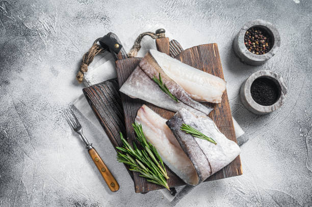 filetto di pesce di eglefino, carne di pesce cruda su tavola di legno con erbe. sfondo bianco. vista dall'alto - fish filet foto e immagini stock