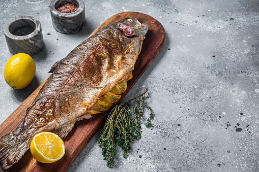 Grilled whole trout, bbq fish on a wooden board with herbs. Gray background. Top view. Free space for your text.