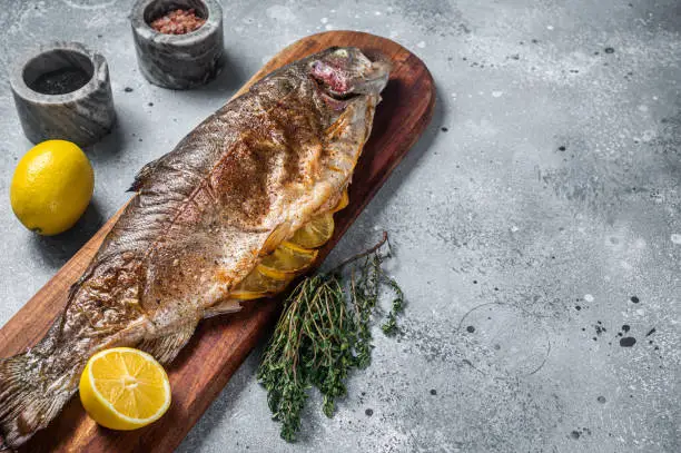 Photo of Grilled whole trout, bbq fish on a wooden board with herbs. Gray background. Top view. Free space for your text