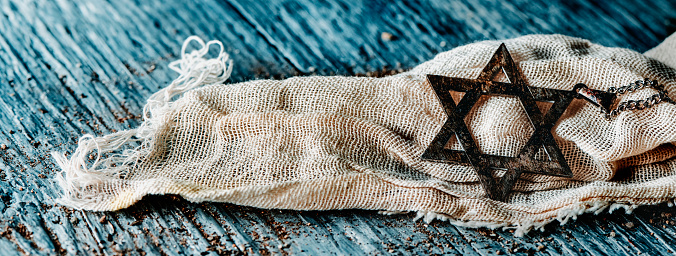 an old pendant in the shape of the star of david, on a ragged piece of cloth, on a gray rustic wooden surface, in a panoramic format to use as web banner